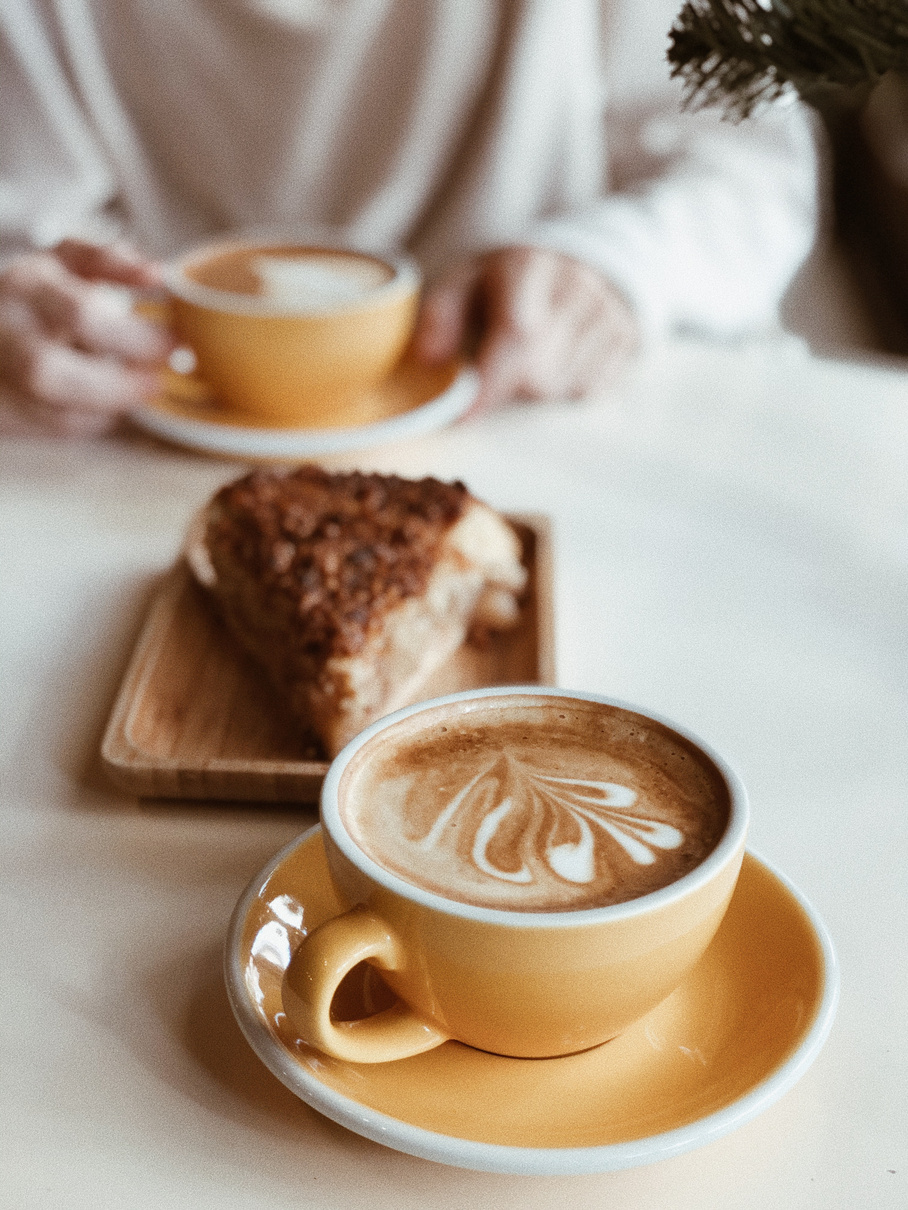 Cup of latte near piece of cake in coffee shop